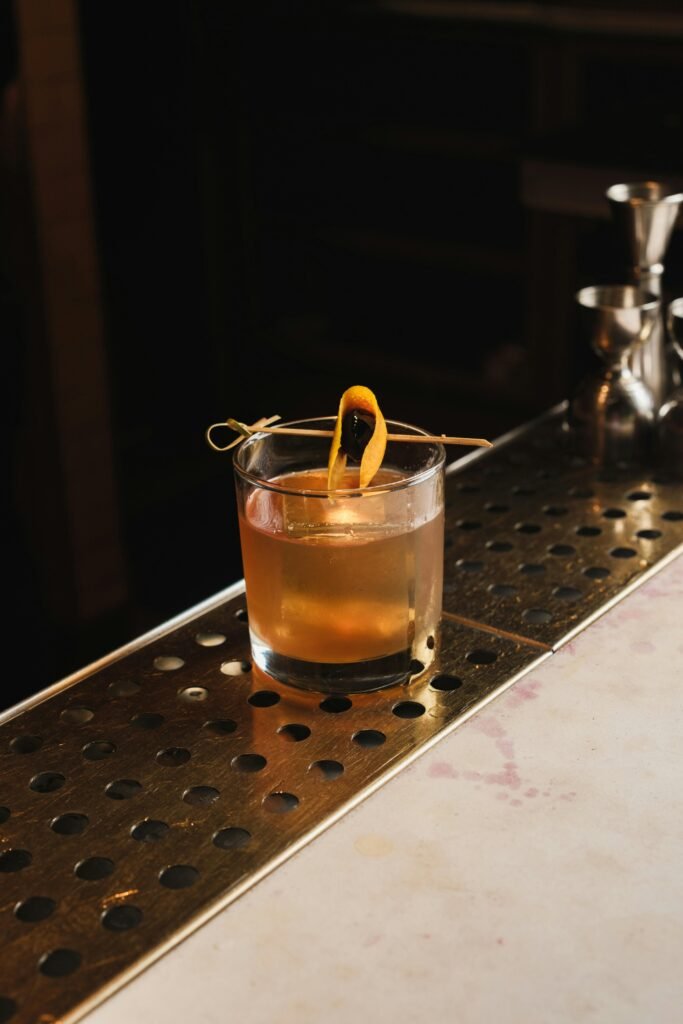 A classic old fashioned cocktail with orange garnish served on a dimly lit bar counter.